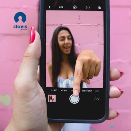 bright pink walled background with a hand holding an iphone in focus. woman jumping out of the screen to press a button on the phone